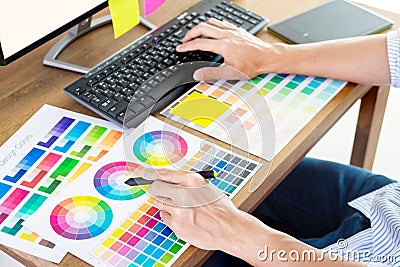 Graphic designer or creative holding Mouse and do his work material color pantone swatch samples art tools at desk in office Stock Photo