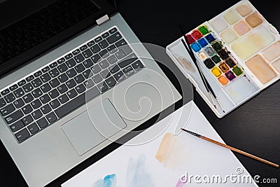 Graphic designer`s desk table, laptop, watercolors palette and sheet for painting on a dark wooden table Stock Photo