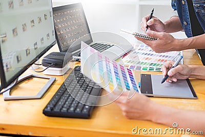 graphic designer team working on web design using color swatches editing artwork using tablet and a stylus At Desks In Busy Stock Photo