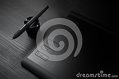 Graphic tablet with pen for illustrators and designers on black wooden background. Stock Photo