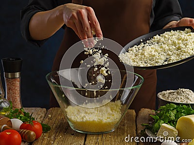 Grated cheese in a glass bowl in frozen flight on a dark background. Vegetables, herbs, eggs, spices on a wooden table. A Stock Photo