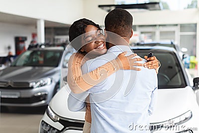 Grateful Black Wife Embracing Husband After Buying New Car In Dealership Showroom Stock Photo