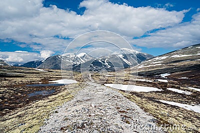 Gravel pathway used as leading lines towards mountain scenery with snow capped mountains and blue sky. Stock Photo