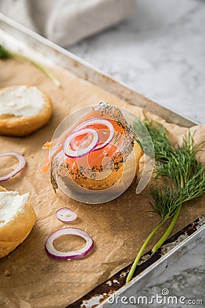 Gravlax a raw, marinated graved salmon with dill on bred roll bun with cream cheese, onion rings on tray with baking paper and Stock Photo