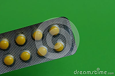 Gray blister with round yellow pills on a green background Stock Photo