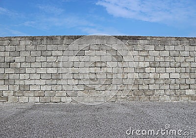 Gray cement block wall with an asphalt street in front and blue sky above. Stock Photo