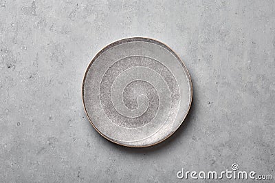 Gray ceramic plate on grey concrete rough background. Empty spotted uneven saucer. Matte dish on stone textured backdrop. Hand Stock Photo