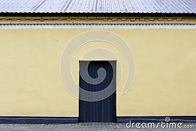 gray door, a wall with beige plaster, a roof, paving slabs Stock Photo
