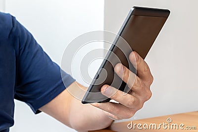 Gray e-reader electronic book in male hand. A man in a blue t-shirt with a tablet Stock Photo