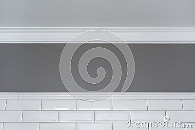 Gray painted wall, white ceiling molding and ceramic decorative tiles small white glossy brick. Fragment of the walls of the bathr Stock Photo
