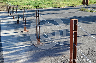 Gray pillars separating the park path from the road. deliberately rusty steel bollards bent into a double space slot connected by Stock Photo