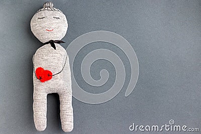 Gray sleeping and smiling handmade doll with red heart in her hands from the threads on gray paper background with copy space Stock Photo