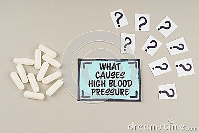 On a gray surface there are question marks and a blue sticker with the inscription - What Causes High Blood Pressure Stock Photo