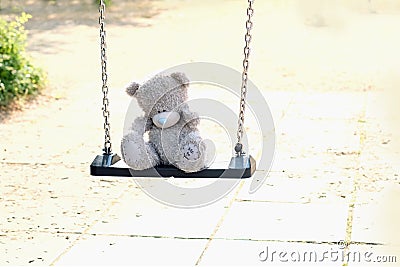 Gray teddy bear sitting alone on swing, concept of loss of parents, loneliness of children, caring for orphans Stock Photo