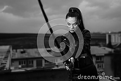 Grayscale of female in black ninja assassin costume holding a sword and standing near wall Stock Photo