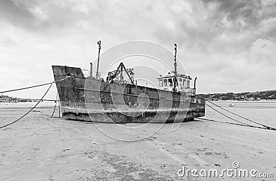 Grayscale of a ferry side abandoned wales boat on the sandy beach, cloudy sky background Stock Photo