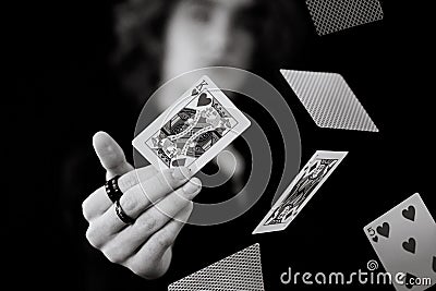 Grayscale shot of a magician holding the king of hearts surrounded by a falling stack of cards Stock Photo