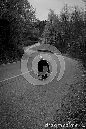 Grayscale shot of a person riding a skateboard on a curvy road in a forest Stock Photo