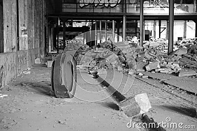 Grayscale shot of a wheel with a pile of debris in the middle of an old, abandoned factory building Stock Photo