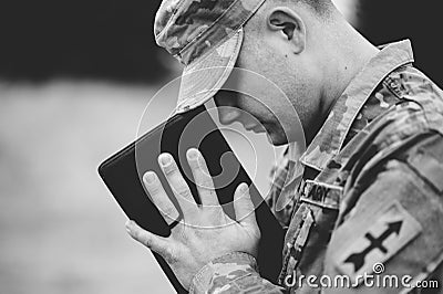 Grayscale shot of a young soldier praying while holding the bible Stock Photo