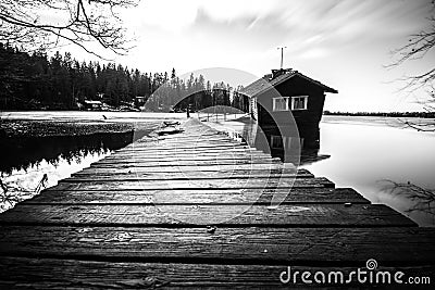 Grayscale of wooden pier land with rural Drunken Sauna in the water with forest trees Stock Photo