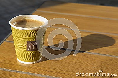 Great coffee in the original paper cup in McDonalds. It is located on a wooden surface. Close-up Editorial Stock Photo