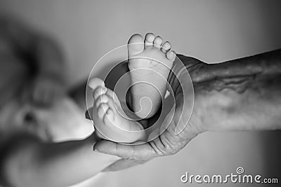 Great-grandmother touching little baby foot, black and white shot, the concept of a family and a new life. into a selective focus Stock Photo