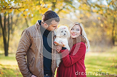 Great time for walk! Beautiful family couple with white cute Maltese dog spending time in autumn park Stock Photo