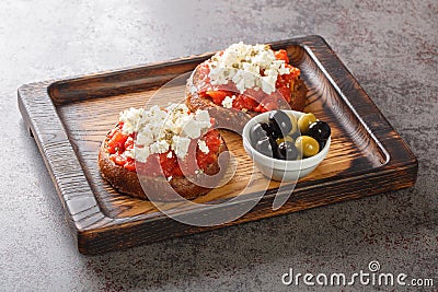 Greek dakos appetizer with barley rusk, tomatoes, feta cheese, oregano and olive oil closeup on the wooden board. Horizontal Stock Photo