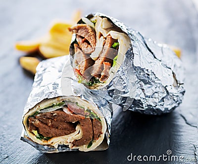 Greek gyro wrapped in foil cut in half and served with fries Stock Photo