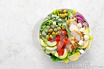 Greek inspired salad with grilled chicken meat, vegetables and feta cheese in a bowl on a table, with olive oil dressing Stock Photo