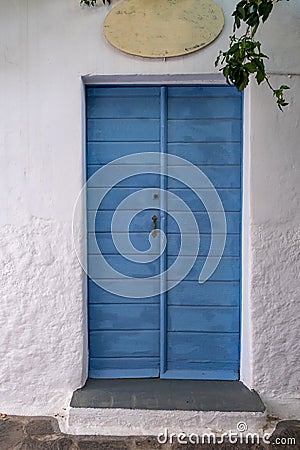 Greek Island, Cyclades. Blue wooden close vintage door against whitewashed stonewall. Vertical Stock Photo