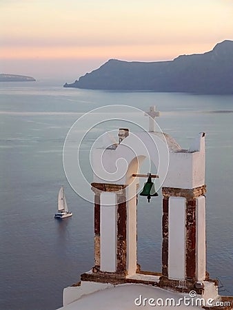 Greek Orthodox Church Bell Tower against Aegean Sea with Sailing Boat at the Sunset, Santorini Stock Photo