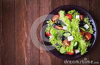 Greek salad (lettuce, tomatoes, feta cheese, cucumbers, black olives) on dark wooden background top view Stock Photo