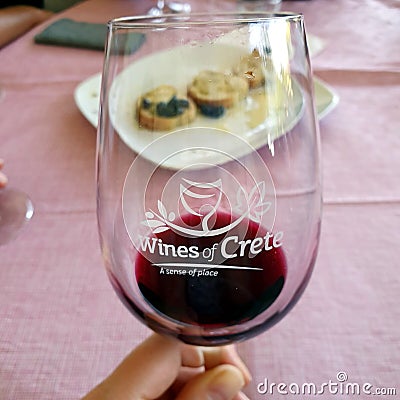 Greek wine tasting. A glass in hand with a bit of red wine. In the background, bread with olive oil Editorial Stock Photo