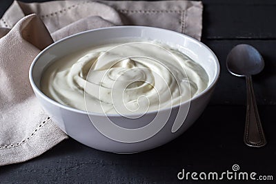Greek yogurt in a white bowl on a rustic black wooden table Stock Photo