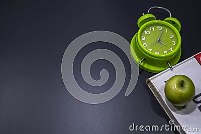 Green alarm clock with green apple on top of the bunch of books Stock Photo