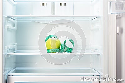 Green apple with measuring tape on shelf of open empty refrigerator Stock Photo