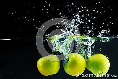 Green apples falling into the water with a splash against black background Stock Photo