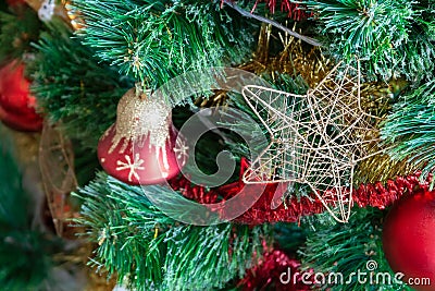 Green artificial Christmas tree decorated with star in a golden frame and interlacing threads; red bell with gold glitter Stock Photo