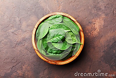 Green baby spinach leaves in wooden bowl on rustic stone table top view. Organic healthy food. Stock Photo