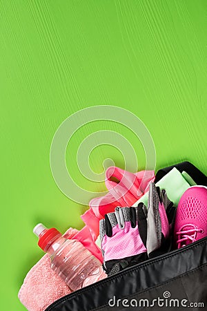 On a green background, a set of female sporting things of pink color in an open bag with a bottle of water Stock Photo