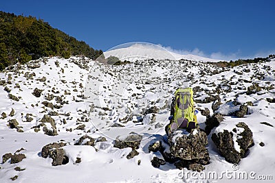 Green backpack on the snow covered volcanic rock of Etna Park Stock Photo