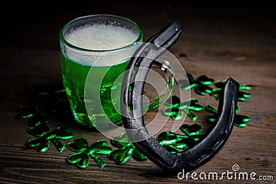 St. Patrick`s Day. Green Beer pint with rusty horseshoe on wooden table, decorated with shamrock leaves. Stock Photo