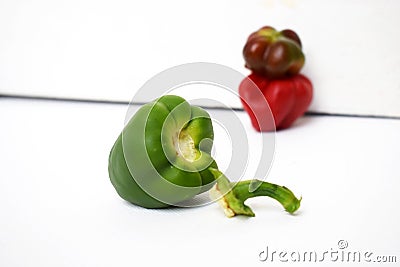 A green bell pepper with its head cut off next to two red bell peppers fade on a white background Stock Photo