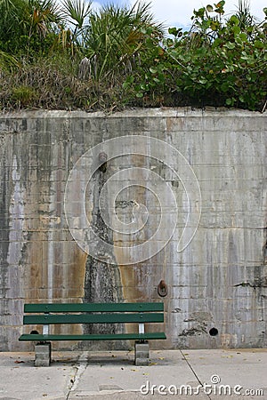 Green bench set against a tall concrete wall Stock Photo