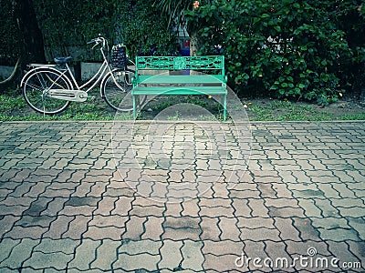 Green benches and bicycles and trees with brown walkway flooring are made of bricks Stock Photo