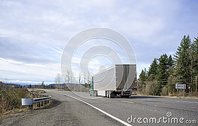 Green big rig semi truck transporting frozen cargo in shine stainless steel refrigerator semi trailer running on the safety road Stock Photo