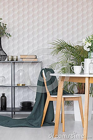 Green blanket on chair at wooden table in dining room interior with plant and wallpaper. Real photo Stock Photo