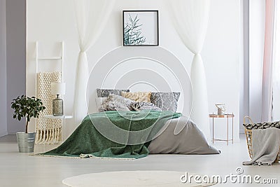 Green blanket thrown on double bed with many pillows and grey sh Stock Photo